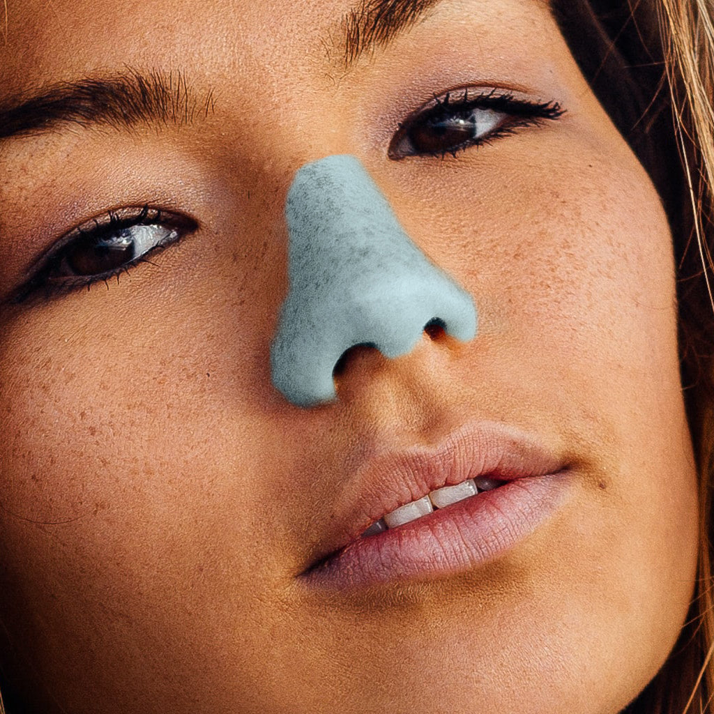 Beautiful girl wearing blue noz reef safe sunscreen lotion on her nose 